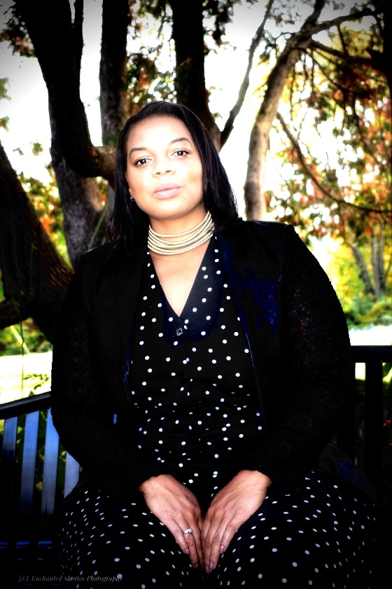 Tiawana Anderson, seated outdoors in a black and white polka-dot dress, black cardigan and silver necklace, facing the camera.